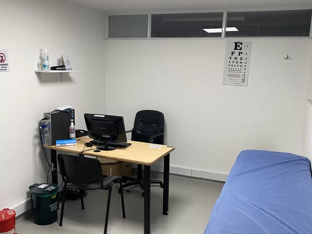 Consultorio con optotipo de Snellen en la pared, escritorio y camilla de examen