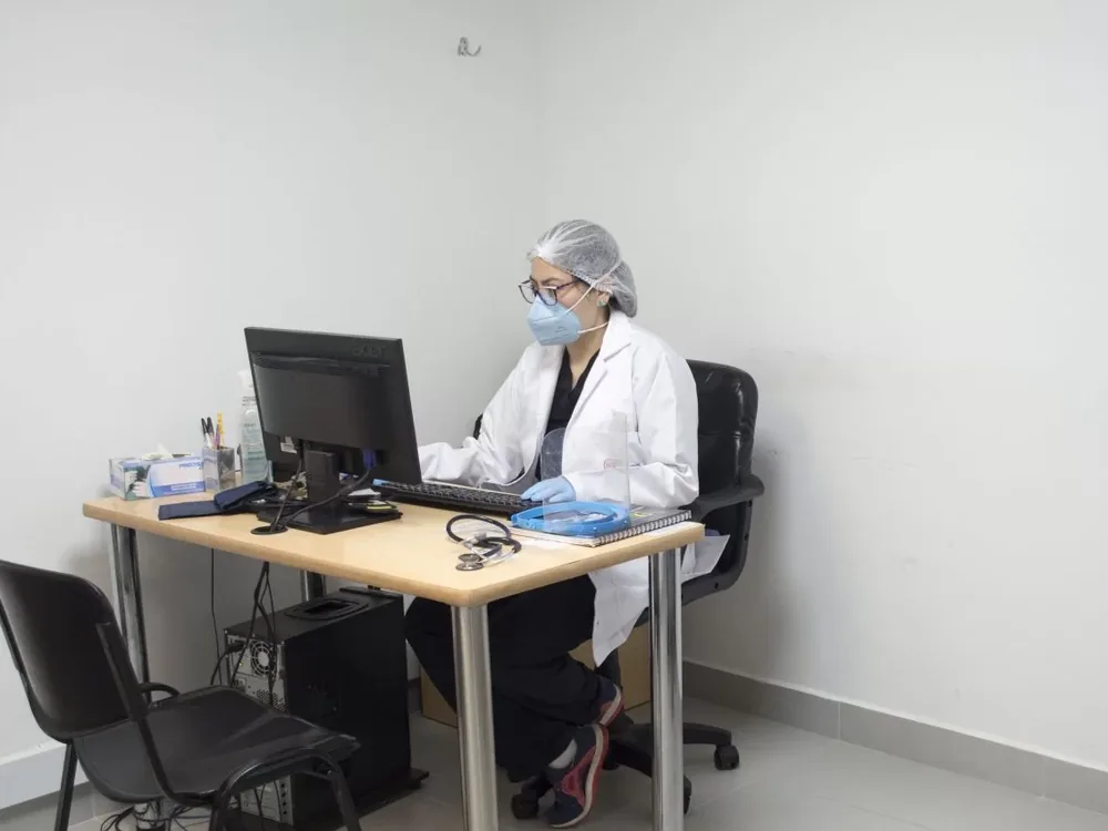 Médica con bata y fonendoscopio registrando la historia clínica ocupacional en el computador